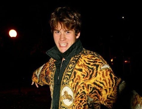 David Tisel wearing a leopard themed coat with their arms outstretched and looking at the camera